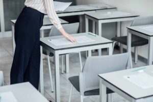 Une femme surveillance dans une salle de concours dépose une copie sur les tables en préparation de l'arrivée des candidats
