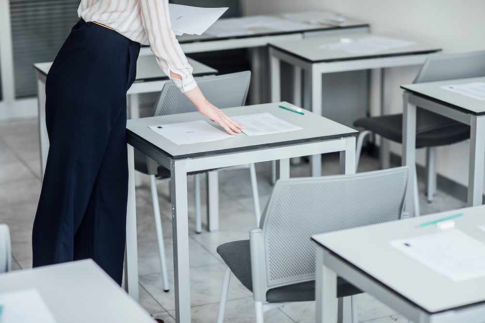 Une femme surveillance dans une salle de concours dépose une copie sur les tables en préparation de l'arrivée des candidats